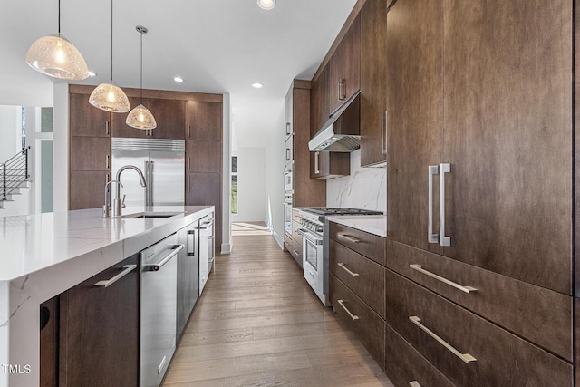 kitchen featuring sink, high end appliances, light wood-type flooring, pendant lighting, and decorative backsplash