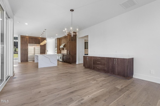 kitchen with pendant lighting, a kitchen island with sink, stainless steel appliances, an inviting chandelier, and light hardwood / wood-style flooring