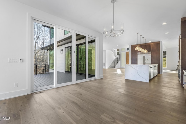 unfurnished living room with sink, an inviting chandelier, and dark hardwood / wood-style flooring