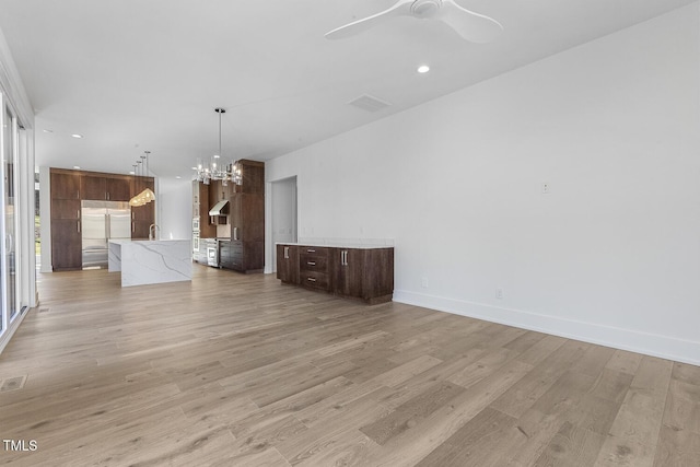 unfurnished living room with ceiling fan with notable chandelier and light hardwood / wood-style flooring