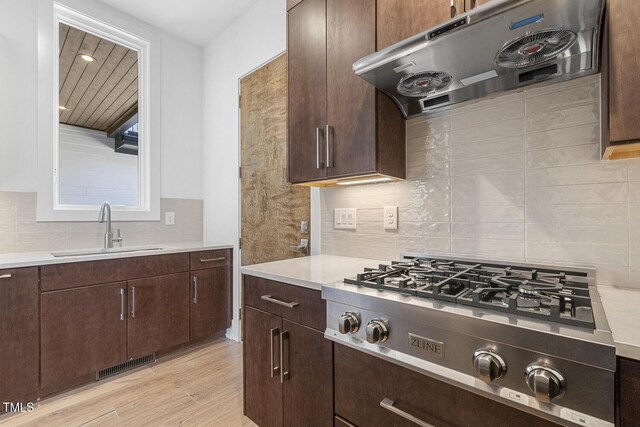 kitchen featuring stainless steel gas stovetop, sink, decorative backsplash, dark brown cabinets, and light wood-type flooring