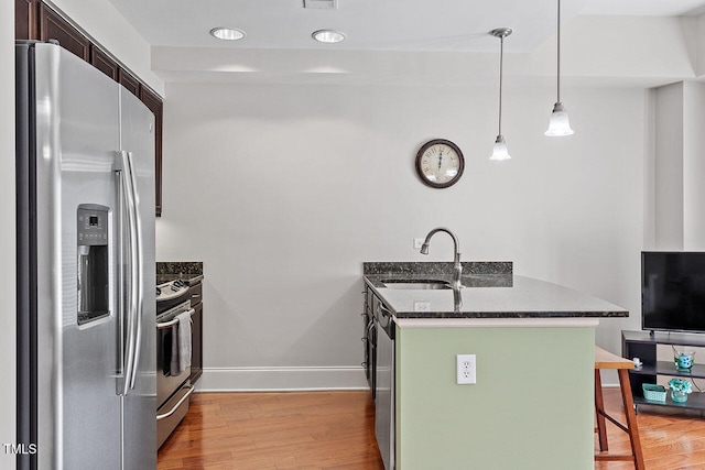 kitchen featuring appliances with stainless steel finishes, a breakfast bar, sink, light hardwood / wood-style floors, and hanging light fixtures