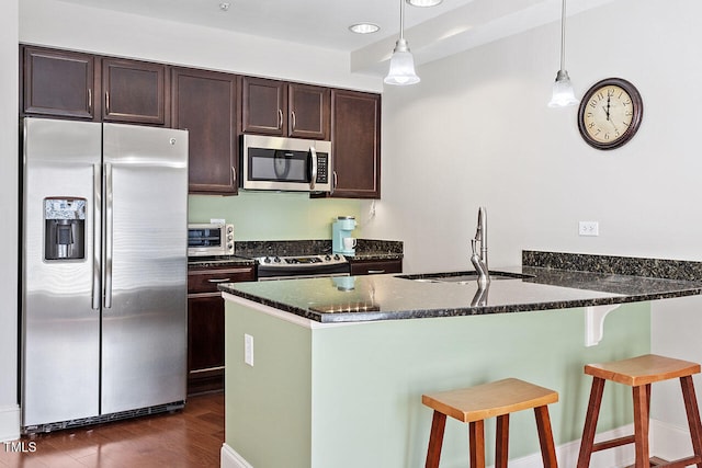 kitchen with pendant lighting, dark stone counters, dark hardwood / wood-style floors, appliances with stainless steel finishes, and kitchen peninsula