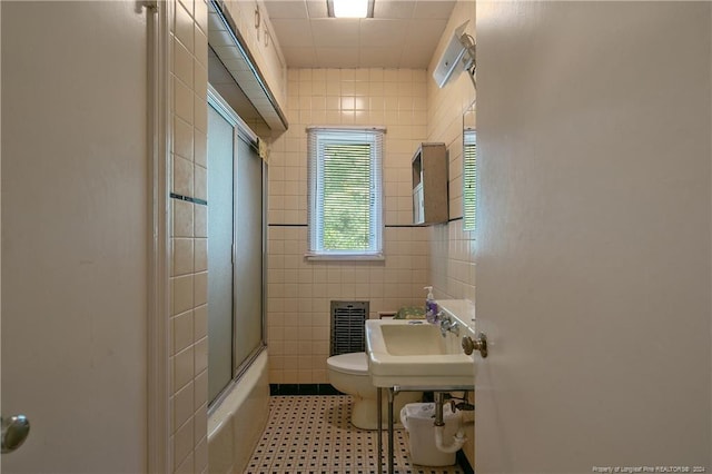 full bathroom featuring toilet, combined bath / shower with glass door, tile walls, and sink