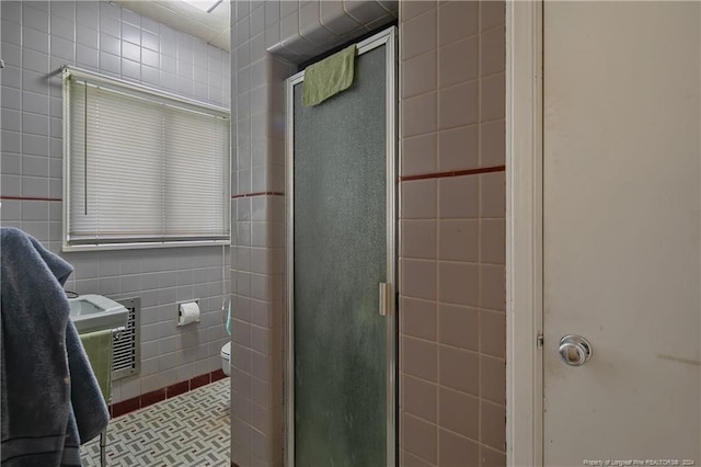 bathroom featuring a shower with door, tile patterned floors, toilet, and tile walls