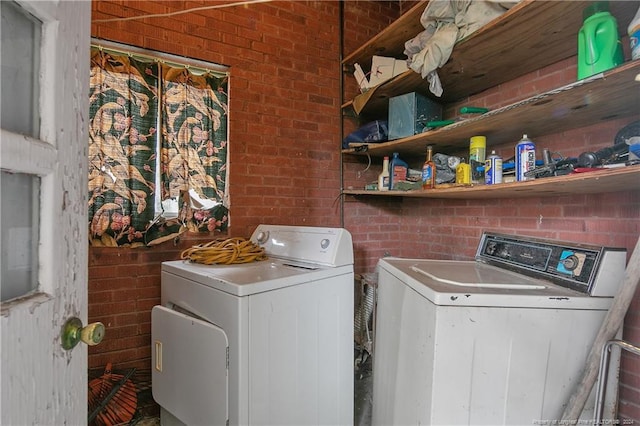 washroom featuring washing machine and dryer and brick wall