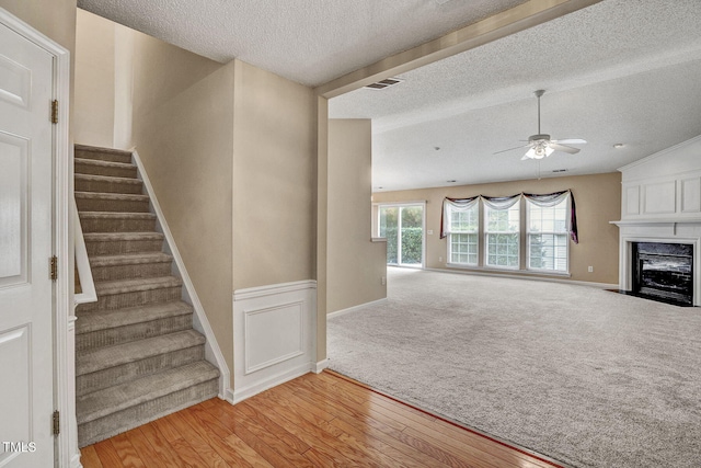 staircase with a textured ceiling, a fireplace, hardwood / wood-style flooring, and ceiling fan