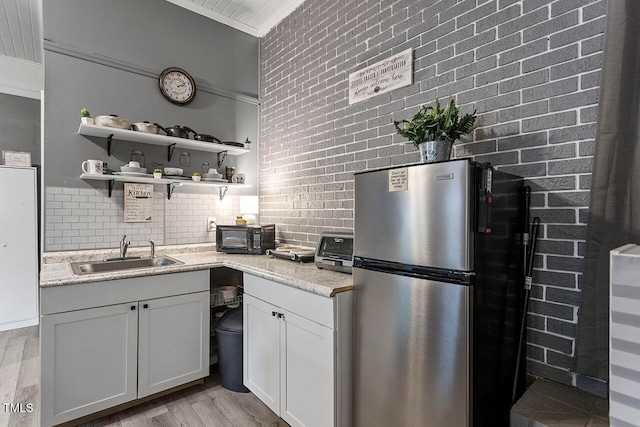 kitchen featuring light stone counters, white cabinetry, sink, and stainless steel refrigerator