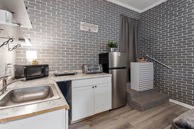 kitchen featuring sink, light hardwood / wood-style flooring, stainless steel fridge, ornamental molding, and white cabinetry