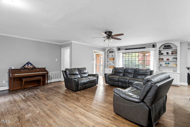 living room with built in shelves, wood-type flooring, ceiling fan, and ornamental molding