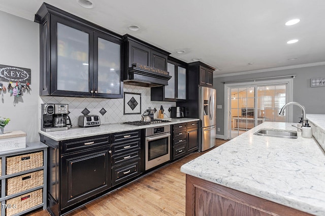 kitchen with tasteful backsplash, stainless steel appliances, crown molding, sink, and light hardwood / wood-style flooring