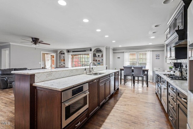 kitchen featuring light stone countertops, dark brown cabinets, stainless steel appliances, sink, and hardwood / wood-style flooring