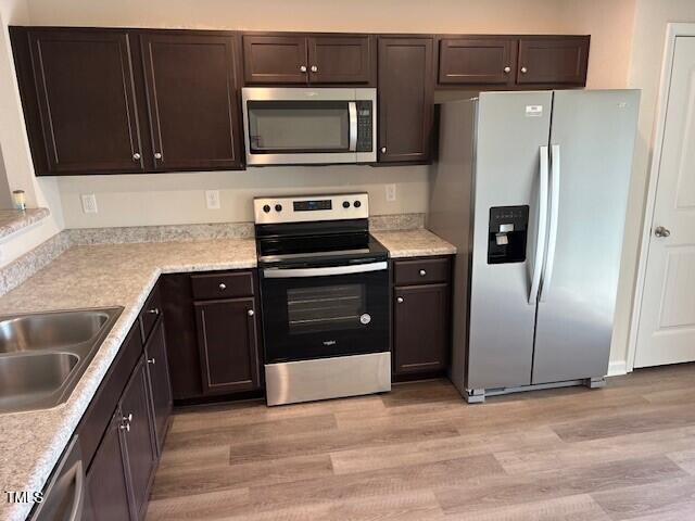 kitchen with dark brown cabinetry, stainless steel appliances, and light hardwood / wood-style floors