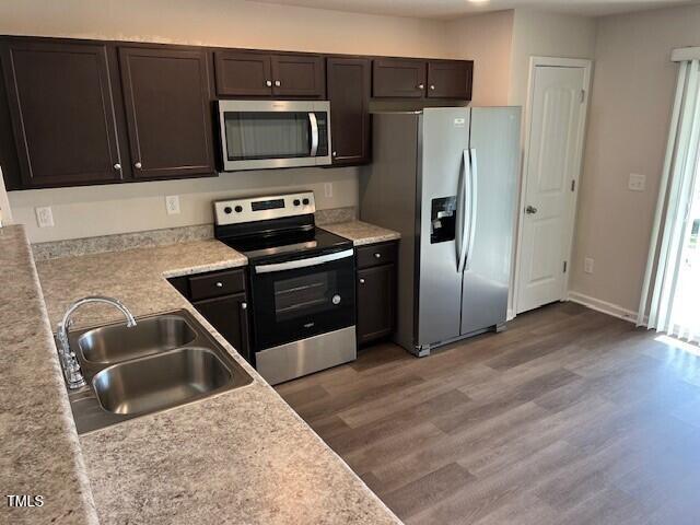 kitchen with hardwood / wood-style floors, sink, dark brown cabinetry, and appliances with stainless steel finishes