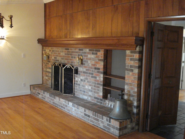 interior details featuring wooden walls, wood-type flooring, ornamental molding, and a fireplace