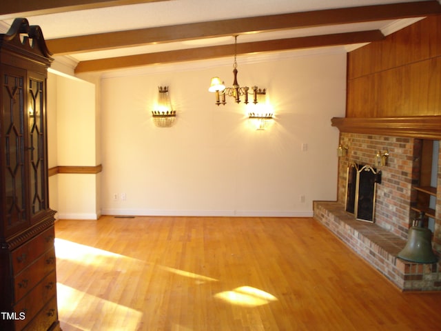 unfurnished living room featuring crown molding, light hardwood / wood-style floors, a brick fireplace, beamed ceiling, and a chandelier