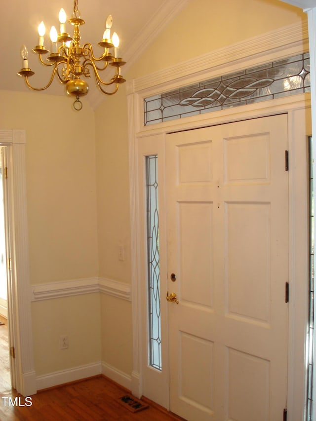 foyer with ornamental molding, a notable chandelier, hardwood / wood-style flooring, and vaulted ceiling