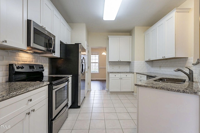 kitchen featuring appliances with stainless steel finishes, white cabinetry, light tile patterned floors, sink, and stone countertops