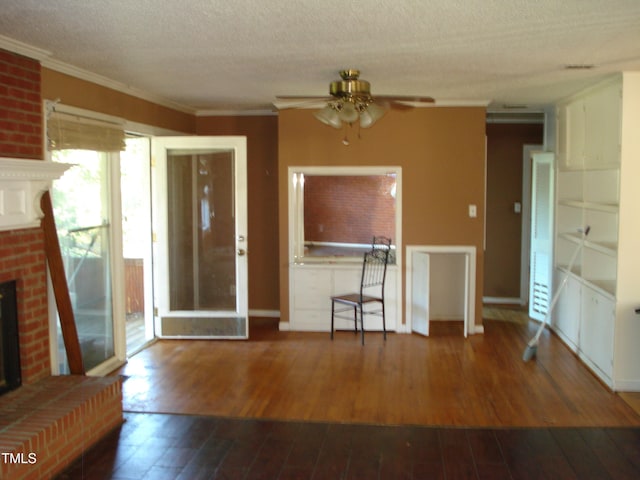 unfurnished living room with ornamental molding, ceiling fan, a textured ceiling, a brick fireplace, and dark hardwood / wood-style flooring