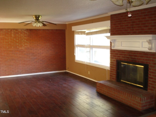 unfurnished living room featuring dark wood-type flooring, ornamental molding, ceiling fan, a fireplace, and brick wall