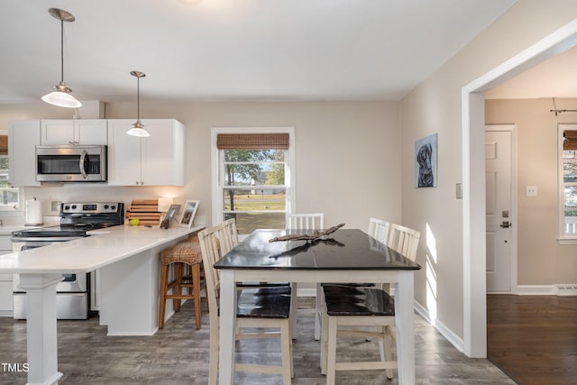 kitchen with a kitchen bar, white cabinets, hanging light fixtures, appliances with stainless steel finishes, and dark hardwood / wood-style flooring