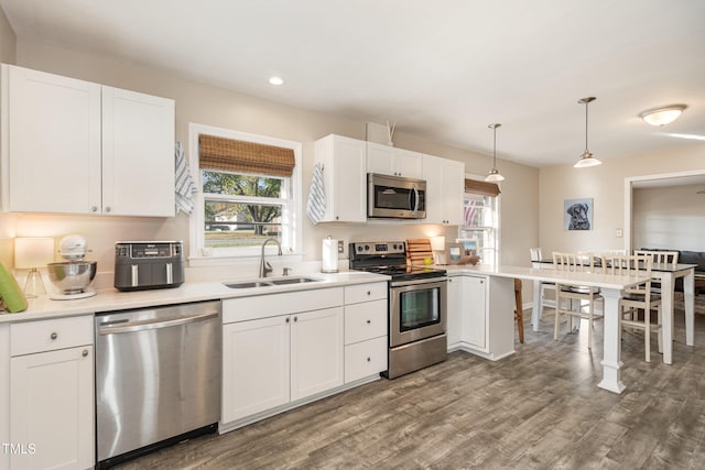 kitchen featuring appliances with stainless steel finishes, sink, pendant lighting, dark hardwood / wood-style floors, and white cabinetry