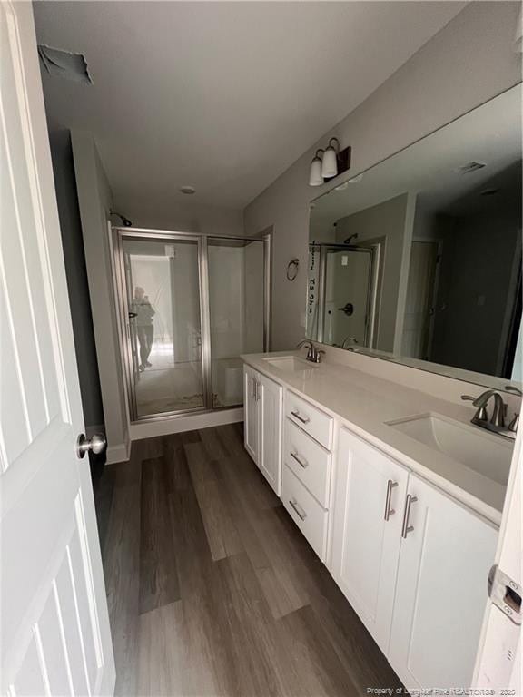 bathroom with double vanity, wood finished floors, a stall shower, and a sink