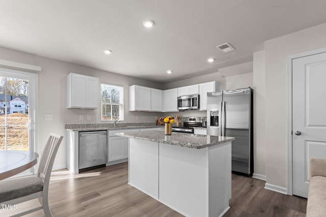 kitchen with white cabinets, a center island, light stone counters, and stainless steel appliances