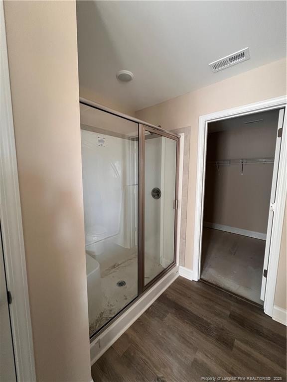 full bath featuring toilet, wood finished floors, visible vents, baseboards, and a shower stall