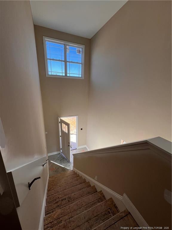 staircase with a healthy amount of sunlight, a high ceiling, baseboards, and wood finished floors