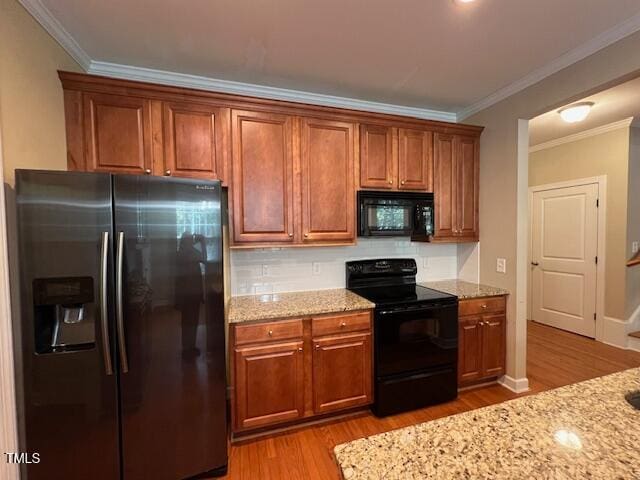 kitchen featuring light hardwood / wood-style floors, light stone countertops, black appliances, and crown molding