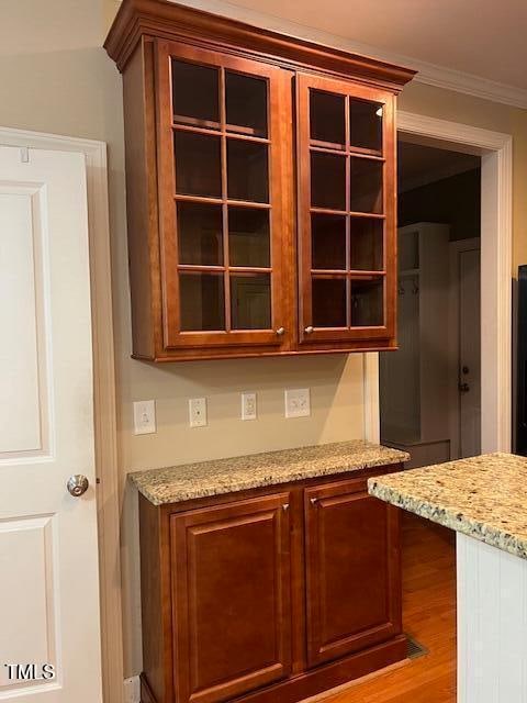 bar with light wood-type flooring, light stone counters, and crown molding