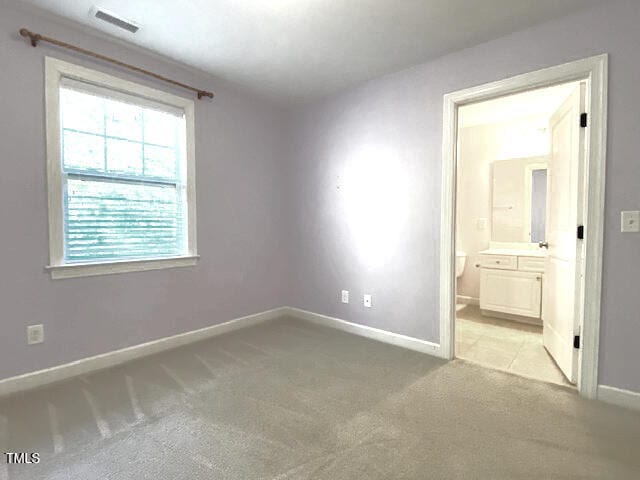 unfurnished bedroom featuring ensuite bathroom and light colored carpet