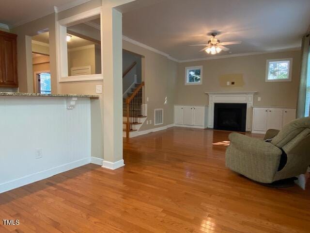 unfurnished living room featuring ceiling fan, a healthy amount of sunlight, light wood-type flooring, and crown molding