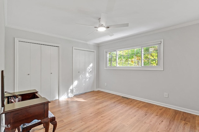 bedroom featuring light wood-type flooring, two closets, ceiling fan, and crown molding