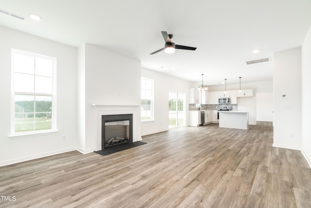 unfurnished living room with ceiling fan, light hardwood / wood-style floors, sink, and a healthy amount of sunlight