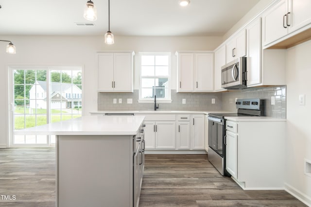 kitchen featuring appliances with stainless steel finishes, backsplash, hanging light fixtures, white cabinets, and dark hardwood / wood-style flooring