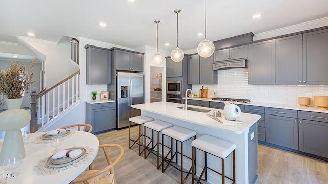 kitchen with ornamental molding, stainless steel appliances, hanging light fixtures, sink, and a kitchen island with sink