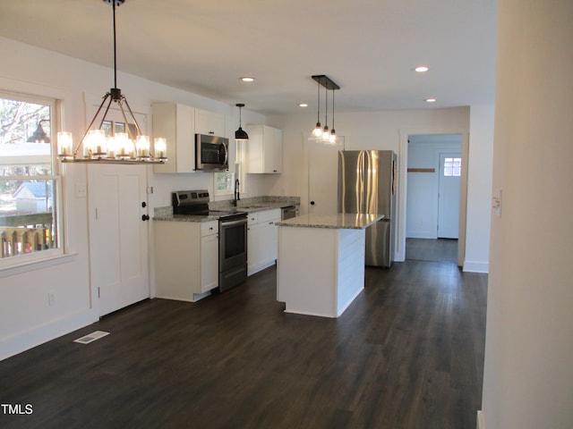 kitchen featuring pendant lighting, appliances with stainless steel finishes, a center island, and dark hardwood / wood-style flooring