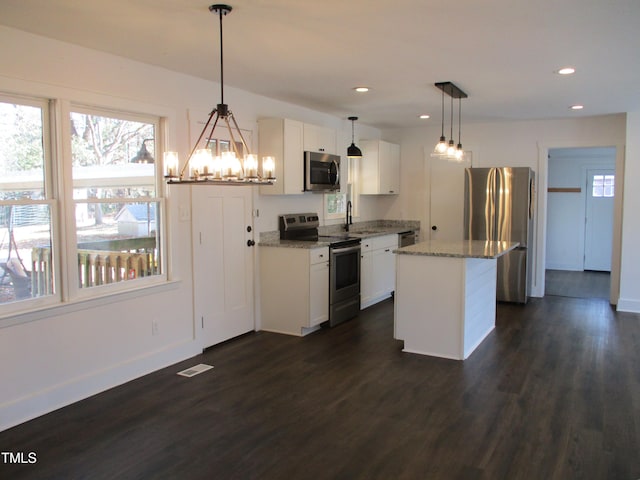 kitchen with stainless steel appliances, hanging light fixtures, white cabinetry, and a kitchen island