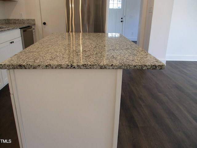 kitchen featuring appliances with stainless steel finishes, dark hardwood / wood-style flooring, light stone countertops, and a kitchen island