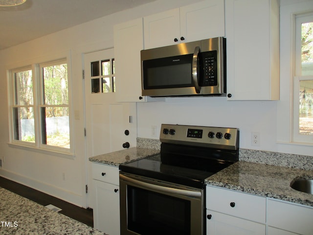 kitchen with stainless steel appliances, white cabinetry, a healthy amount of sunlight, and light stone counters