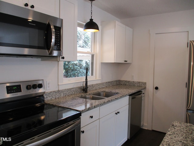 kitchen with white cabinetry, sink, light stone counters, appliances with stainless steel finishes, and pendant lighting