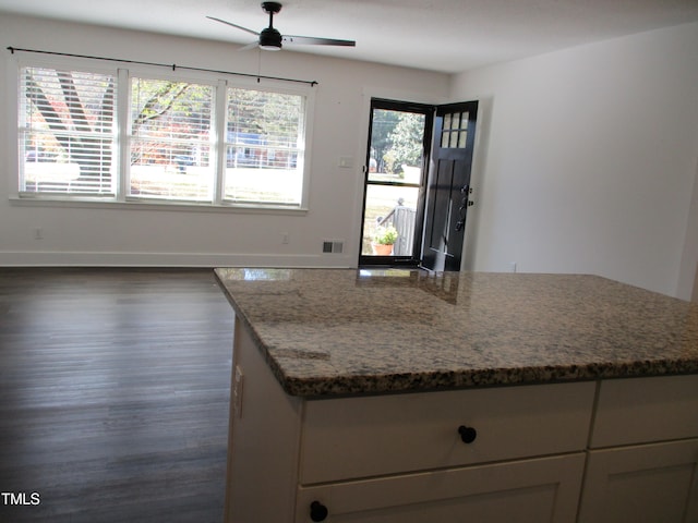 kitchen featuring dark wood-type flooring, light stone countertops, ceiling fan, and a kitchen island