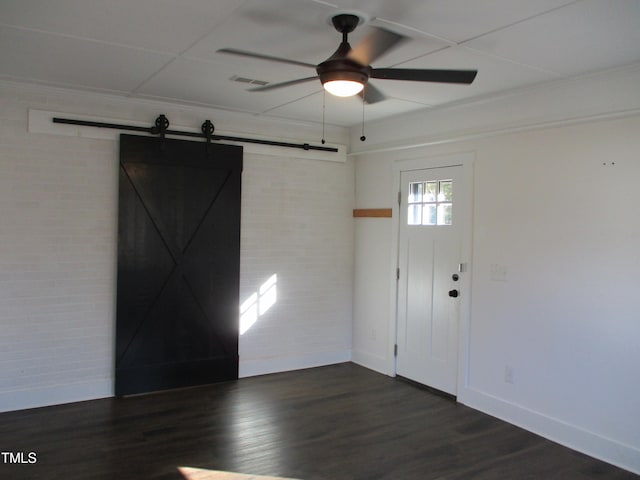 entryway featuring brick wall, a barn door, dark hardwood / wood-style floors, and ceiling fan