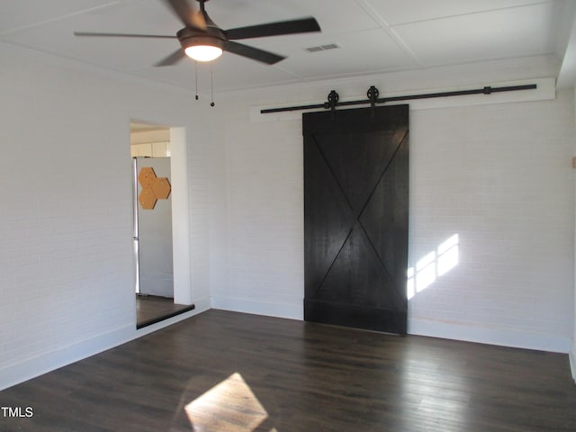 spare room with dark wood-type flooring, a barn door, crown molding, and brick wall