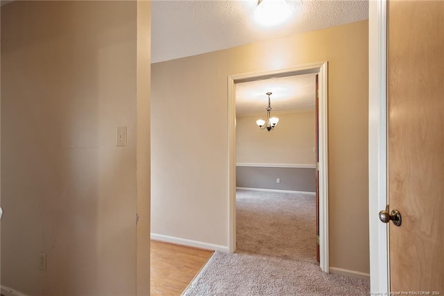 hallway featuring an inviting chandelier, a textured ceiling, and light colored carpet