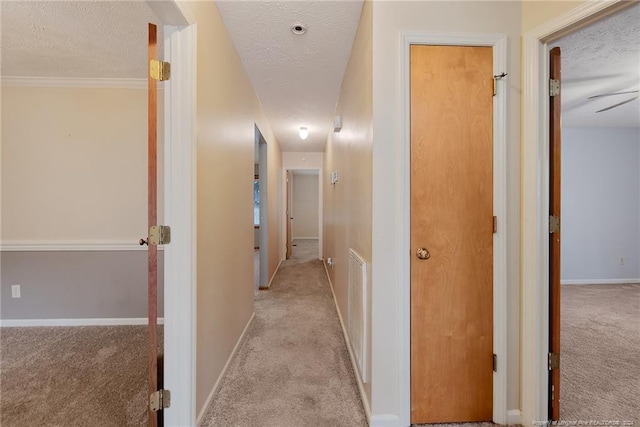 hall with light colored carpet, a textured ceiling, and ornamental molding