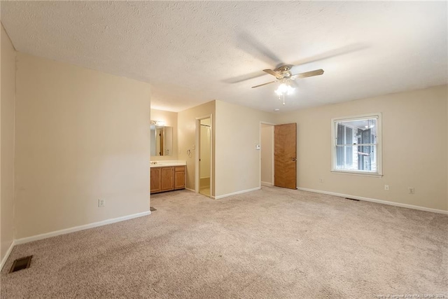 unfurnished bedroom with a textured ceiling, light carpet, ceiling fan, and connected bathroom