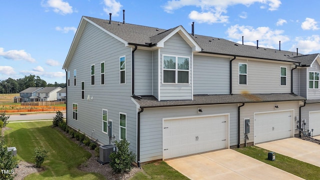 rear view of property featuring a garage, a lawn, and central AC